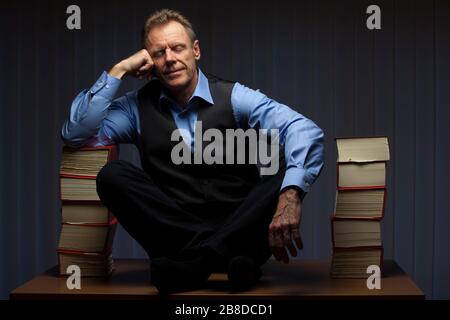 Anwalt oder Geschäftsmann entspannen sich spät in der Nacht auf einem Schreibtisch mit vielen Büchern in einem dunklen Büro Stockfoto