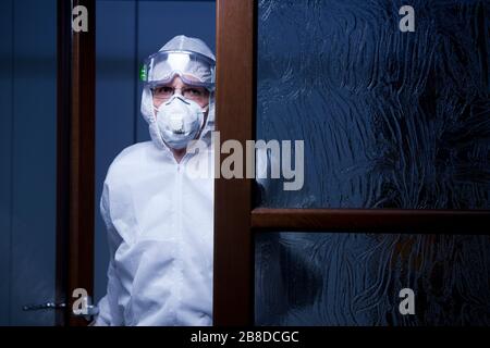 Müder Arzt, der die Kamera am Eingang eines Krankenhauses mit Schutzkleidung betrachtet - nachts mit dunkelblauem Hintergrund aufgenommen Stockfoto