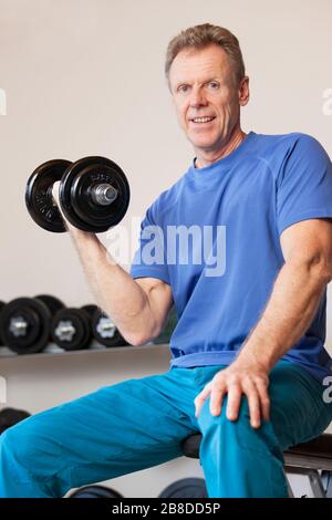 Passen Sie den reifen oder älteren Mann, der beim Gewichtheben mit einem Lächeln auf die Kamera lächelt - konzentrieren Sie sich auf das Gesicht Stockfoto