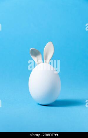 Osterei mit Bunny-Ohren auf blauem Hintergrund. Kreative Grußkarte. Minimalitätskonzept. Kopieren Sie Speicherplatz Für Ihren Text Stockfoto