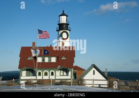 Auf dem Turm des Leuchtturms Portland Head, dem ältesten Leuchtfeuer in Maine, wird während der Ferienzeit ein großer Kranz angezeigt. Amerikanische Flaggenwellen während einer Windy Stockfoto