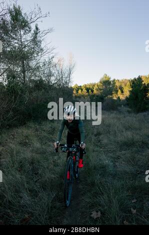 Radfahrerin fährt mit Sonnenuntergang in der Waldbahn auf die Kamera zu Stockfoto