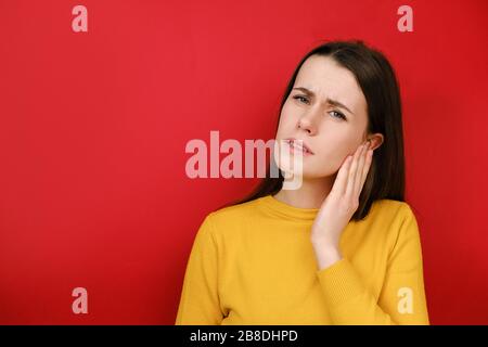 Ungesunde junge Frau, die an starkem Ohrschmerzen leidet. Gestresstes schauerndes Mädchen, das das Ohr verstopft, schmerzhafte Beschwerden spürt, schlechten Klang vermeidet, gelb trägt Stockfoto