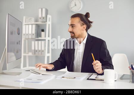 Der Geschäftsmann in einer schwarzen Jacke funktioniert. Analysen am Computer im Büro. Stockfoto