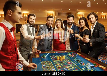 Fröhliche Freunde mit Sektgläsern, die lächeln, während sie Casino-Poker-Roulette spielen. Stockfoto