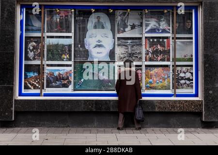 Moskau, Russland. Am 21. März 2020 sieht sich eine alte Frau Fotos der TASS-Nachrichtenagentur für 2019 an der Fassade des Agenturgebäudes im Zentrum Moskaus, Russland, an Stockfoto