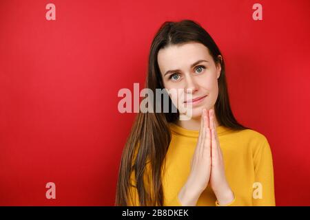 Schöne attraktive junge Frau verbindet Hände in betende Geste mit Hoffnung, ziemlich nettes junges Mädchen bitten Hilfe und Unterstützung, Blick auf die Kamera Stockfoto
