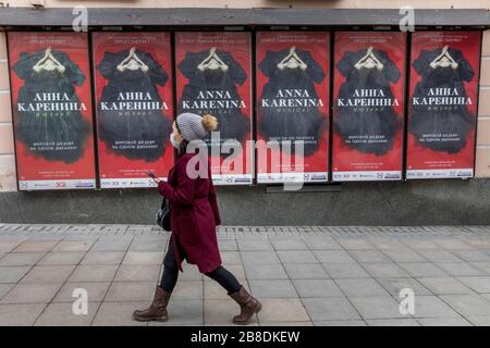 Moskau, Russland. März 2020 EINE Frau in einer medizinischen Maske, die auf dem Hintergrund der Theaterplakate Musical Anna Karenina in der Innenstadt von Moskau, Russland, die Straße hinunterläuft. Schulen, Museen und Theater wurden landesweit während der Epidemie des Coronavirus COVID-19 geschlossen, und Versammlungen von mehr als 50 Menschen wurden in Moskau verboten Stockfoto