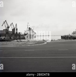 1964, historischer, weiter entfernter Blick auf die drei Trichterschiffe, die British Ocean Liner, RMS Queen Mary, die an den Docks in Lorient, Bretagne, Frankreich, festmachte. Die Queen Mary war ein Passagierschiff, das die Transatlantikroute bediente und diesen Markt bis zur Ankunft des Düsenflugzeugs Ende der 1950er Jahre dominierte. Gebaut in den 1930er Jahren von John Brown & Co in Clydebank, Schottland für den damals bekannten "Cunard-White Star", operierte es von 1936 bis 1967 und konnte über 2.000 Passengers befördern. Während des 2. Weltkriegs wurde sie zu einem Troopschiff umgebaut und verbannte Verbündete. Stockfoto