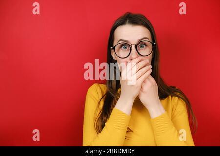 Verängstigte Frau in Brillen schaut auf Kamera macht große Augen, die Mund mit Händen entsetzt fühlen, Frau erhielt schockierende Nachrichten posieren Stockfoto