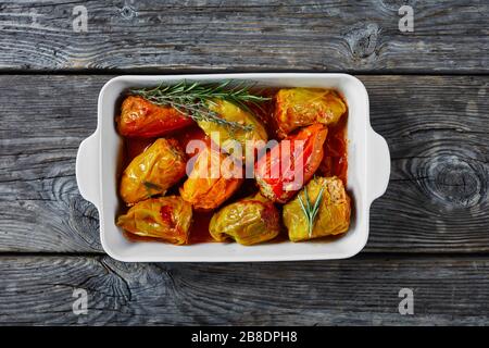 Süße Paprika gefüllt mit Reis und Hackfleisch: Rindfleisch und Schweinefleisch mit Tomatensauce, Rosmarin und Thymian, kafelige Gewürze auf einer Backform, auf einem Holzrücken Stockfoto