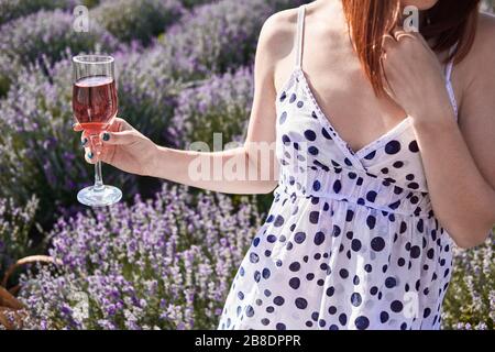 Blendung der Sonne in einem Glas Rosengwein. Auf den Lavendelfeldern hält eine Frau das Glas Wein an der Hand Stockfoto