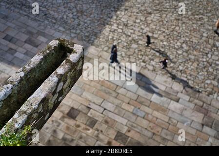 Drei unfokussierte Menschen und ihre Schatten auf dem Kopfsteinpflaster der Plaza del Obradoiro in Santiago de Compostela, Galicien von einem Balkon des c Stockfoto