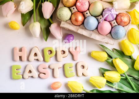 Ostergrüßkarte mit Tulpenblumenmuster, ostereiern und Kaninchenplätzchen. Draufsicht über weißen Marmortisch Stockfoto