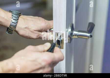 Mann Reparatur des Türknopfes mit Schraubendreher, die Hand des Mitarbeiters, die neue Türverriegelung installiert Stockfoto
