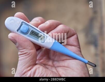 Die männliche Hand hält klinisches Thermometer mit Koronatext auf dem Bildschirm während der globalen Kovid-19- oder Corona-Pandemie Stockfoto