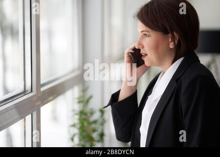 Geschäftsfrau hat Telefongespräch in der Nähe des Bürofensters. Manager, Arbeitgeber. Stockfoto