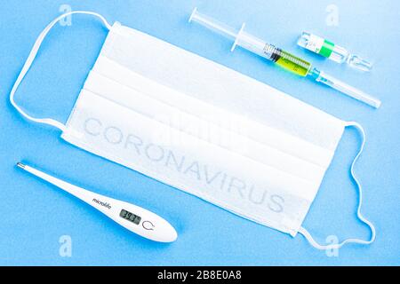 Flache, schützende medizinische Gesichtsmasken, Digitalthermometer mit hoher Temperatur und verstreuten Pillen und Spritze auf blauem Hintergrund. Stockfoto