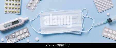 Verschiedene Arten schützende medizinische Gesichtsmaske, Pillen, Thermometer auf Blau. Ansicht von oben. Vorbeugung gegen Viren. Leerzeichen für Text. Banner. Stockfoto