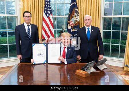 Der US-Präsident Donald Trump, der sich von Vizepräsident Mike Pence und Finanzminister Steven Mnuchin zusammenschloss, hält die unterzeichnete Kopie von H.R. 6201, dem "Families First Coronavirus Response Act", im Oval Office des Weißen Hauses am 18. März 2020 in Washington, DC. Stockfoto
