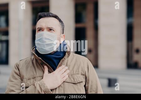 Außenschuss eines kranken Mannes trägt eine medizinische Maske gegen Viren, hat Atemnot und Husten, fühlt sich unwohl an, schützt vor Coronavirus, kümmert sich um h Stockfoto