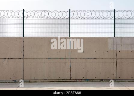 Rasierdraht mit seinen scharfen Stahlbarben auf einer Betonwand Stockfoto