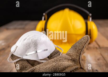 Schutzmaske, die von einem Lederhandschuh gehalten wird. Schutzzubehör für den Produktionsarbeiter. Dunkler Hintergrund. Stockfoto