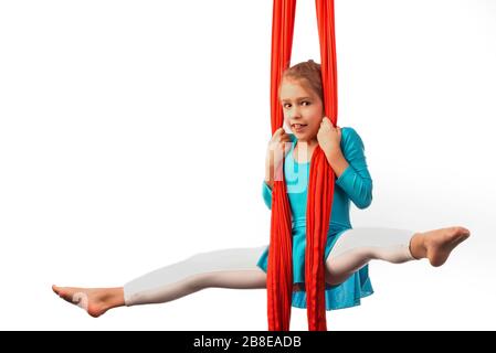 Kleines acrobat Mädchen, das sich in der Luft spaltet und an einem roten Luftband auf weißem Hintergrund hält. Akrobatikkonzept. Werbefläche Stockfoto