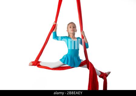 Kleines acrobat Mädchen, das sich in der Luft spaltet und an einem roten Luftband auf weißem Hintergrund hält. Akrobatikkonzept. Werbefläche Stockfoto