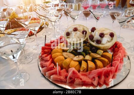 Festlicher Tisch mit kalten exotischen alkoholischen Getränken, Cocktails, Wassermelone, Trauben, Bananen und verschiedenen frischen Früchten. Feier oder andere Veranstaltung Stockfoto