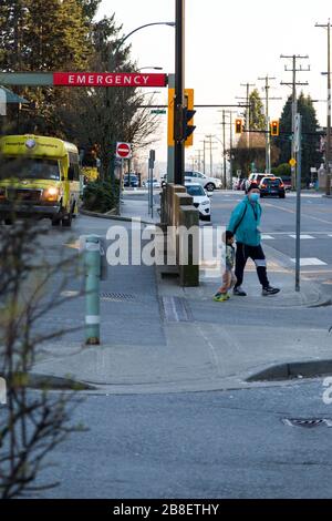 NORTH VANCOUVER, BC, KANADA - MAR 19, 2020: Ein Vater trägt eine medizinische Gesichtsmaske vor dem Notfalleingang des Lions Gate Hospital während des Jahres 2020 Stockfoto