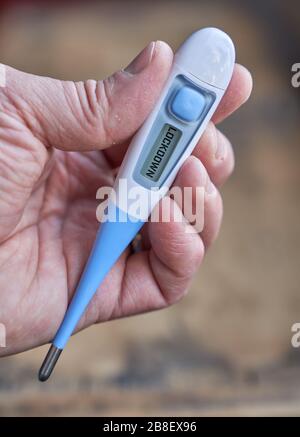 Die männliche Hand hält klinisches Thermometer mit Sperrtext auf dem Bildschirm während der globalen Kovid-19- oder Corona-Pandemie Stockfoto