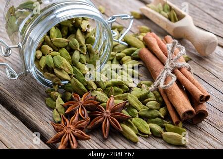 Becher mit grünen Kardamom-Pads. Zimtstangen, Kardamomsamen, Holzschaufel und Anissterne auf dem Tisch. Stockfoto