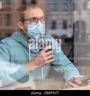 Der Mann Tragt Schutzmaske Trinkt Kaffee Durch Ein Strohhalm In Einer Maske Im Cafe Benutzt Smartphone Und Liest Nachrichten Uber Die Situation Mit Coronavirus Stockfotografie Alamy