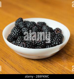 Eine weiße Schüssel mit saftigen Brombeeren, die auf einem Holzhintergrund isoliert ist, schließt Platz ein Stockfoto