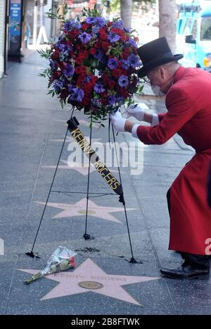 Hollywood, Kalifornien, USA. März 2020. GREGG DONOVAN in einem formellen roten Mantel und Schwanz, weiße Handschuhe, sowie einen Hut, der wegen Coronavirus eine Gesichtsmaske trägt, platziert einen Blumenstrauß mit schönen roten Rosen Blumen und Schildern auf einer Karte, Als Kranz wird am Samstag der Star von Kenny Rogers auf dem Hollywood Walk of Fame platziert. Die langjährige Gesangslegende und der Schauspielstar starben am späten Freitag im Alter von 81 Jahren. Kredit: Ringo Chiu/ZUMA Wire/Alamy Live News Stockfoto