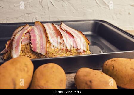 Fleischbrot mit Speckscheiben. Hausgemachte Fleischbraten auf Bratpfanne. Kartoffelforegraund. Stockfoto