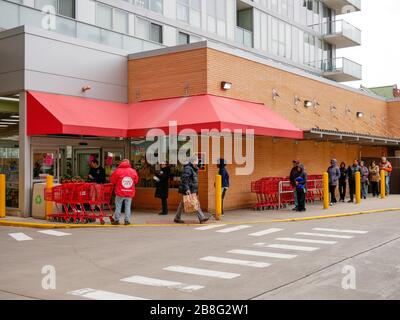 Oak Park, Illinois, USA. März 2020. Einkäufer legen sich außerhalb eines Lebensmittelgeschäftes von Trader Joe an und halten Abstand zwischen ihnen als präventive Maßnahme gegen die Verbreitung von COVID-19. Gouverneur Pritzker hat einen "Helter in Kraft"-Befehl implementiert, der heute um 17 Uhr Ortszeit in Kraft treten soll. Stockfoto