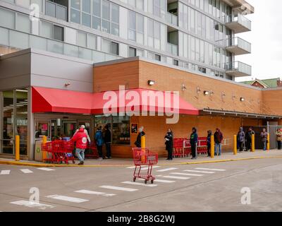 Oak Park, Illinois, USA. März 2020. Einkäufer legen sich außerhalb eines Lebensmittelgeschäftes von Trader Joe an und halten Abstand zwischen ihnen als präventive Maßnahme gegen die Verbreitung von COVID-19. Gouverneur Pritzker hat einen "Helter in Kraft"-Befehl implementiert, der heute um 17 Uhr Ortszeit in Kraft treten soll. Stockfoto