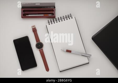 Minimalistischer Hintergrund im Arbeitsbereich mit Laptop, Stift, Stifttasche, Armbanduhr und offenem Notebook. Weißer Büroschreibtischrahmen. Arbeiten, Geschäft, freiberufliche Zusammenarbeit Stockfoto