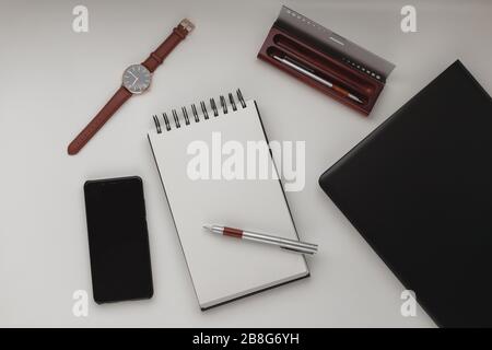 Minimalistischer Hintergrund im Arbeitsbereich mit Laptop, Stift, Stifttasche, Armbanduhr und offenem Notebook. Weißer Büroschreibtischrahmen. Arbeiten, Geschäft, freiberufliche Zusammenarbeit Stockfoto