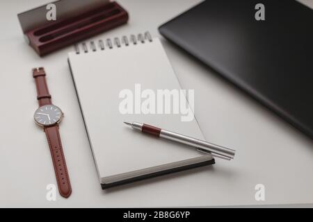 Hoher Betrachtungswinkel eines offenen Spiralnotizbuchs mit einem leeren Blatt und einem Hintergrund am Arbeitsplatz. Laptop, Stift, Stifttasche und Uhr. Arbeiten, Geschäft, Freiberufler Stockfoto