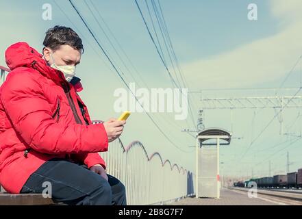 Der Mann in einer antiviralen medizinischen Maske sitzt auf einer Bank auf der Plattform Stockfoto