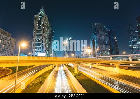 Lange Exposition von Autos, die nachts auf der Autobahn vor Wolkenkratzern Dubai - VAE fahren Stockfoto