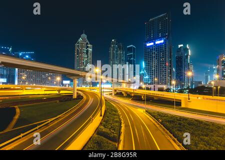 Lange Exposition von Autos, die nachts auf der Autobahn vor Wolkenkratzern Dubai - VAE fahren Stockfoto