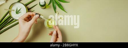 Pipettieren Sie mit kosmetischem CBD-Öl in weiblichen Händen auf grünem Hintergrund mit Kosmetik, Creme mit Cannabis- und Hanfblättern, Marihuana Banner Stockfoto