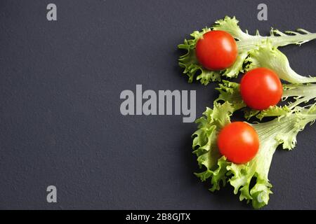 Kirschtomaten und Salat liegen auf einer dunklen Oberfläche. Reife Kirschtomaten. Tomaten sind auf dem Tisch. Tomate in Scheiben geschnitten. Halbierte Kirschtomaten. Stockfoto