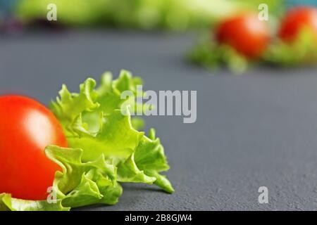 Kirschtomaten und Salat liegen auf einer dunklen Oberfläche. Reife Kirschtomaten. Tomaten sind auf dem Tisch. Tomate in Scheiben geschnitten. Halbierte Kirschtomaten. Stockfoto