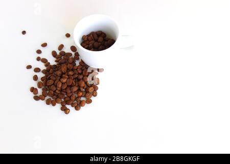 Verschüttete Kaffeebohnen aus dem weißen Keramikbecher isoliert auf weißem Hintergrund Stockfoto