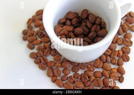 Verschüttete Kaffeebohnen aus dem weißen Keramikbecher isoliert auf weißem Hintergrund Stockfoto